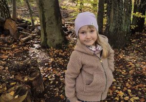 Dziewczynka pozuje do zdjęcia na tle jesiennego lasu.