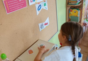 Dziewczynka stoi przed tablicą i próbuje przyczepić element układanki.