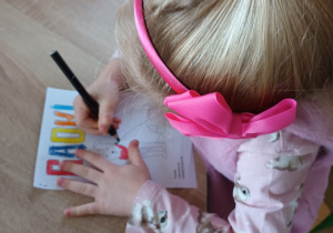 Dziewczynka siedzi przy stole i maluje kolorowankę.