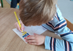 Chłopiec siedzi przy stole i maluje kolorowankę.