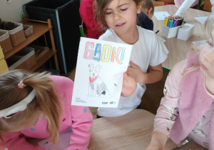 Dziewczynka prezentuje kolorowankę z napisem GADKI oraz psem.