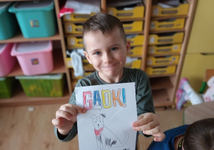 Chłopiec prezentuje kolorowankę z napisem GADKI oraz psem.
