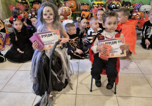 Na pierwszym planie znajduje się chłopiec i dziewczynka, którzy zwyciężyli w konkursie na najciekawszy kostium. W tle znajdują pozostałe dzieci.