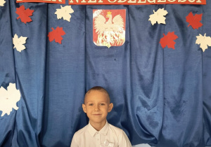 Chłopiec pozuje do zdjęcia na tle dekoracji przygotowanej z okazji Narodowego Święta Niepodległości.