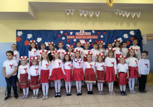 Grupa dzieci pozuje do zdjęcia na tle dekoracji przygotowanej z okazji Narodowego Święta Niepodległości.