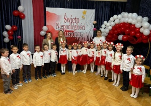 Dzieci wraz z nauczycielkami pozują do zdjęcia w Młodzieżowym Domu Kultury na tle dekoracji przygotowanej z okazji Narodowego Święta Niepodległości.