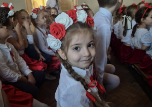 Dziewczynka w odświętnym stroju pozuje do zdjęcia siedząc na widowni Młodzieżowego Domu Kultury.