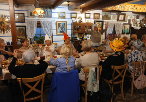 stara chata, przy stole siedzą uczestnicy wyjazdu do "Gniazda" , na głowach mają śmieszne nakrycia