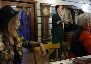 wnętrze starej chaty, przy stole siedzą uczestnicy wyjazdu do "Gniazda", słuchająhistorii tego miejsca opowoadanej przez właścicielkę