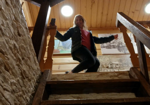 wnętrze chaty, strome drewniane schody, jedna z uczestniczek wyjazdu do felicjanowa stoi na ich szczycie i uśmiecha się