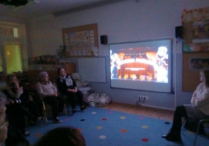 zajęcia warsztatowe z seniorami, grupa siedzi w kole i ogląda prezentację multimedialną