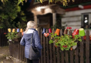 uczestniczka projektu stoi przy płocie, w tle stara chata Gniazda w Felicjanowie