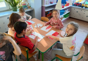 grupa dzieci przy stoliku w klasie, wykonująfarbami pracę plastycznę - polską flagę