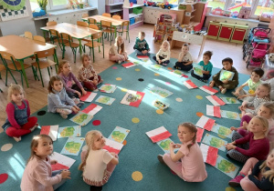 grupa dzieci siedzi na dywanie, przed każdym z nich leżą wykonane prace nawiązujące do święta NIepodległości