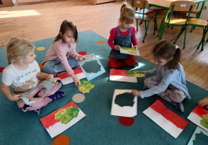 kilkoro dzieci siedzi na dywanie, wypychają kontur Polski z książki