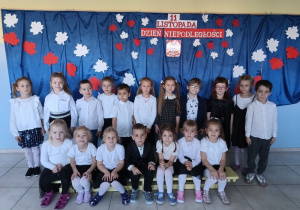 grupa dzieci ubranych na galowo, stoi na tle dekoracji z okazji święta niepodległości, pozują do zdjęcia