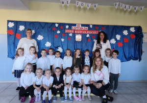 nauczycielki i grupa dzieci ubranych na galowo, stoi na tle dekoracji z okazji święta niepodległości, pozują do zdjęcia