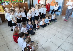 w szatni przedszkolnej zgromadzone dzieci i nauczycielki, wszyscy ubrani na galowo, dzieci mają biało-czerwone wianki , przygotowują siędo wspólnego śpiewania hymnu