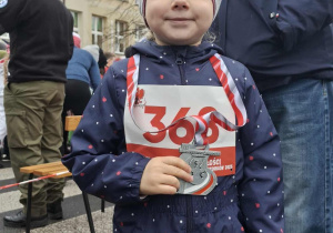 dziewczynka - uczestniczka biegu z okazji Dnia Niepodległości , w ręce ma dyplom, na szyi medal