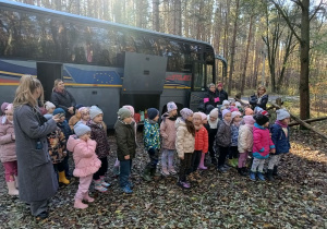 grupa dzieci i nauczycielki w lesie, stoją przed autokarem