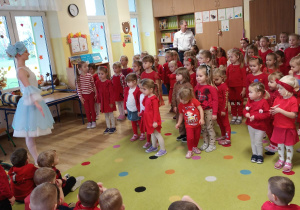 przedszkolaki zgromadzone w klasie, stoją a naprzeciwko nich jest artystka, która pokazuje ruchy taneczne, a dzieci powtarzają