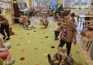 dzieci w klasie siedzą na dywanie, w rekach mająmisie, biorąudział w zajęciach, wszystkie mają takie same koszulki