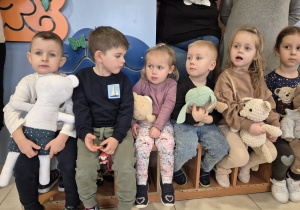 mała grupa dzieci z misiami w dłoniach siedzi na ławce w szatni