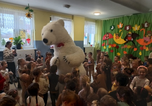 dzieci zgromadzone w szatni, tańczą razem z duzym białym misiem