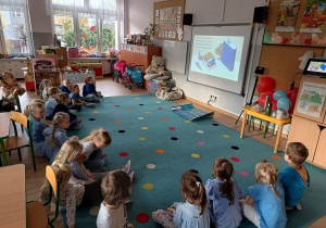 dzieci siedząna dywanie w klasie, oglądają prezentację multimedialną o prawach dziecka