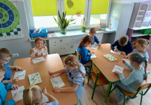 dzieci zgromadzone przy stolikach, malują niebieskimi farbami kontury serca