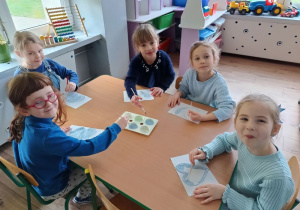 dzieci zgromadzone przy stolikach, malują niebieskimi farbami kontury serca