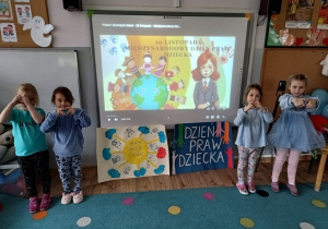 cztery dziewczynki stoją przy tablicy multimedialnej, na której wyswietlony jest slajd z napisem "międzynarodowy dzień praw dziecka"