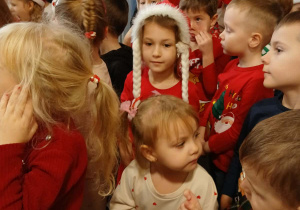 grupa dzieci w przedszkolnej szatni, ubrane na czerwono, niektóre mają mikołajkowe i świąteczne elementy ubioru