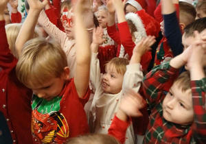 grupa dzieci w przedszkolnej szatni, ubrane na czerwono, klaszcząw ręce, niektóre mają mikołajkowe i świąteczne elementy ubioru
