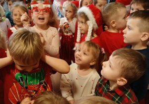 grupa dzieci w przedszkolnej szatni, ubrane na czerwono, niektóre mają mikołajkowe i świąteczne elementy ubioru