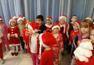 grupa dzieci w przedszkolnej szatni, ubrane na czerwono, niektóre mają mikołajkowe i świąteczne elementy ubioru