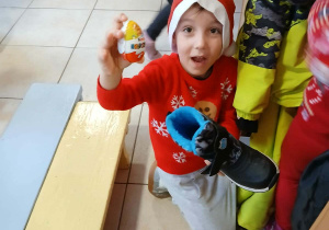 chłopiec w czapce Mikołaja, w jednej ręce ma but, w drukiej niespodziankę którą z niego wyciągnął