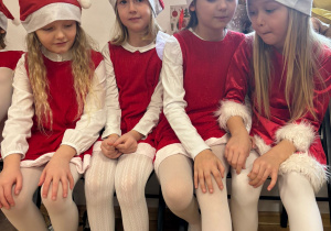 kilka dziewczynak w mikołajkowych sukienkach siedzi na ławce, czeka na wystep