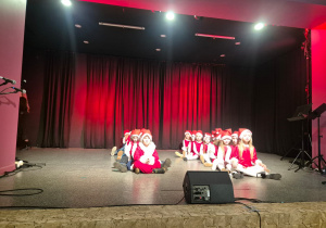 dzieci w mikołajowych strojach na scenie w MOK, siedzą w dwóch rzędach,