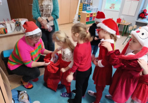 dzieci stoją w kolejce po prezenty, które rozdaje z czerwonego worka nauczycielka w czapce Mikołaja