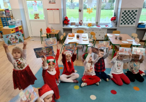 dzieci ubrane w mikołajkowe akcenty, podnoszą niespodzianki które otrzymały od Mikołaja