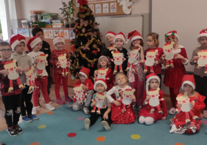 grupa dzieci ubranych na czerwono, niektóre mają mikołajowe czapki, inne swiateczne okulary, itp. pozują do zdjęcia z przy choince