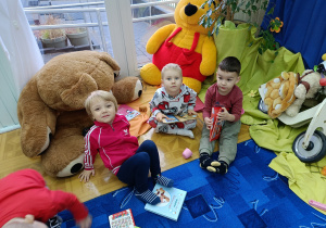 trzech chłopców oglądaksiażęczki, obok nich wielkie pluszowe misie