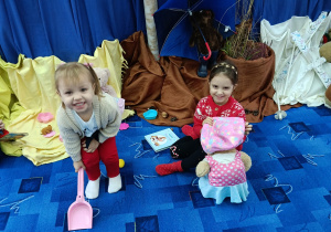 dwie dziewczynki w bibliotece, jedna trzyma lalkę, druga szpadelek