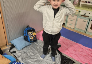 Chłopiec pozuje do zdjęcia. Ma na sobie strój kota. W tle znajdują się śpiwory.