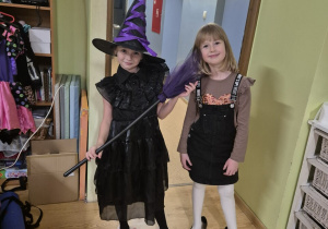 Dwie dziewczynki pozują do zdjęcia. Jedna z nich ma na sobie strój czarownicy.