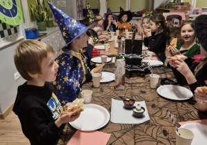 Dzieci siedzą przy stolikach i zjadają pizze na kolację.