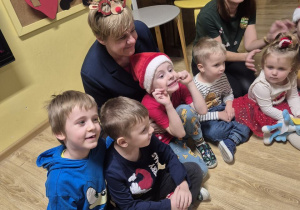 Dzieci wraz z rodzicami siedzą w kole i uczestniczą w świątecznej zabawie.