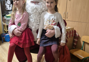 Dwie dziewczynki siedzą na kolanach u Mikołaja i pozują do zdjęcia.