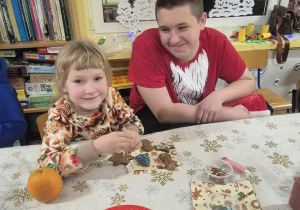 Brat z siostrą siedzą przy stole i ozdabiają pierniczki.